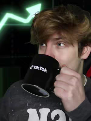 A young man is seen in a close-up shot, holding a black mug with the TikTok logo toward his face. He appears to be taking a sip, with his eyes looking upwards and to the right. Behind him, a blurred, green-colored upward-pointing arrow graphic suggesting growth is visible, set against a dark background. The man is wearing a gray sweatshirt.