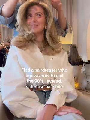A woman with blonde, voluminous 90s-style hair sits in a salon chair. A hairdresser's hands are visible, working on her hair. Text overlayed on the image reads 'Find a hairdresser who knows how to nail the 90's, layered, volumise hairstyle'.