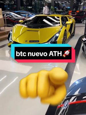 The image features a vibrant yellow Lamborghini parked inside a showroom. The car is the main focus, with sleek lines and a low profile. In the foreground, there's a gesture with a yellow hand pointing directly at the viewer. The background shows other vehicles and an interior, with bright overhead lighting. A text overlay reads 'btc nuevo ATH' with a rocket emoji.