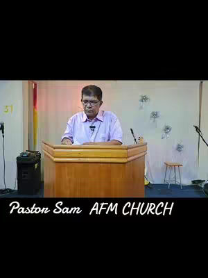 The image features a man in a light purple shirt standing behind a wooden podium in what appears to be a church. The background includes a neutral-colored wall, some decorative floral elements, and a microphone. The bottom of the image displays the text 'Pastor Sam AFM CHURCH'.