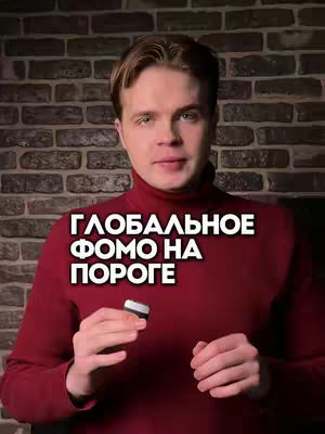 A man in a red turtleneck sweater is the focal point of the image, set against a dark brick wall background. The man is fair-skinned with light brown hair and is smiling. Text overlay in bold white font reads: "ГЛОБАЛЬНОЕ ФОМО НА ПОРОГЕ". He holds a small, rectangular object in his left hand.