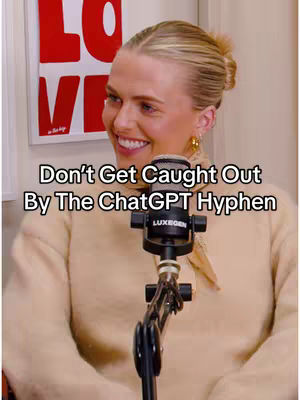 A woman with blonde hair smiles, positioned in front of a microphone. Behind her is a wall with a framed artwork that says 'LO' in red letters. Text overlayed on the image reads: "Don't Get Caught Out By The ChatGPT Hyphen"