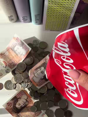 The image shows an open red Coca-Cola can pouring out coins and banknotes onto a white surface. There are also labeled containers in the background. The composition is a mix of textures and shapes, with a focus on the money spilling out.