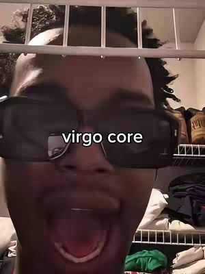 A selfie-style shot with a person with sunglasses and mouth open. There is a text overlay that says 'virgo core.' The person appears to be behind a gray metallic object. Background including neutral color wall and some shelves with objects on them.