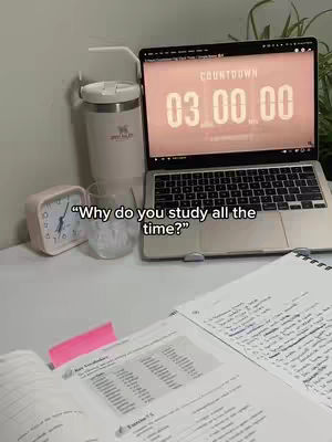 A desk setup with a laptop displaying a timer on screen, a pink alarm clock, a tumbler and a glass. The image has a clean, well-lit composition.