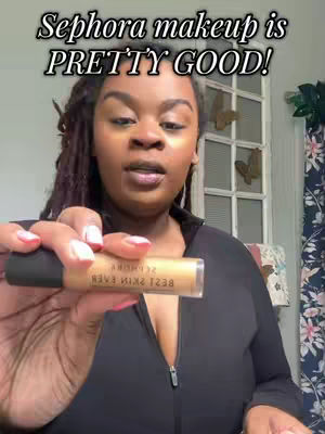 A woman with locs and holding a Sephora makeup product poses for the camera. Overlay text says "Sephora makeup is PRETTY GOOD!". Room decor and a floral curtain are background.