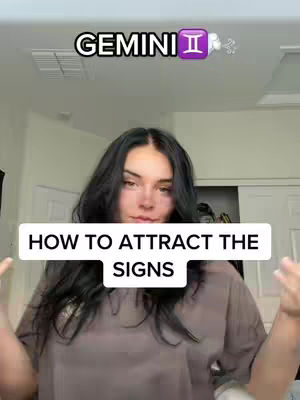 A woman in a taupe shirt stands in front of a light-colored wall with an overhead light, arms opened. The text overlay says 'HOW TO ATTRACT THE SIGNS'. The background is simple, with a door or closet visible behind her.