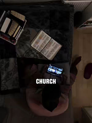 Overhead shot of a person lying on a bed, surrounded by religious items like a Bible, books, and a tablet. The lighting is dim, and the color palette is muted, with browns, blacks, and pinks dominating the scene. A text overlay 'CHURCH' is added on the image.