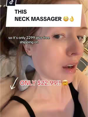 A close-up shot of a fair-skinned woman with red hair, looking at the camera with a slightly open mouth. Above her, a white rectangular bar with black text reads "THIS NECK MASSAGER", supplemented with small emojis. Below, text and an arrow point towards the lower-left, with the price "ONLY $22.99!!" in red and yellow.