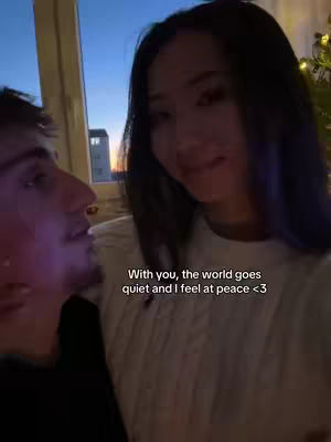 A couple is embracing indoors, with soft lighting and a partially visible window in the background at dusk. The primary focus is on a woman looking at the image viewer and a man embracing her, with overlaid text.