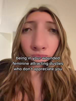 A close-up shot of a young woman with long blonde hair, looking directly at the camera with a slightly distorted fisheye lens effect. Text overlayed on the image reads 'being in your wounded feminine attracting dusties who don't appreciate you'.