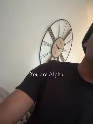 The image shows a person wearing a black t-shirt and a black hat standing near a clock on the wall. The text overlayed reads: "You are Alpha".