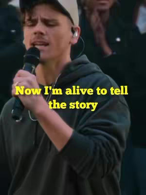 The cover image features a man singing into a microphone, with a text overlay. The man is wearing a hoodie and a cap, with an earpiece. The background is dark, with a blurred crowd.