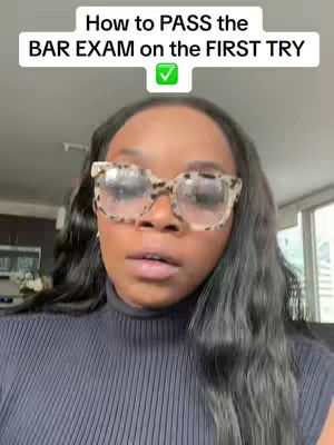 A woman with long dark hair and large eyeglasses is centered in the frame. Above her head, text reads 'How to PASS the BAR EXAM on the FIRST TRY' within a white rectangle, next to a green check mark. She appears to be talking directly to the camera, in front of a blurred background.