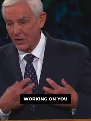 A man in a dark suit and white shirt is addressing the camera, gesturing with his hands. A text overlay reads, "WORKING ON YOU."