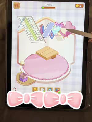 The image displays a tablet screen showcasing a room design game. The game interface features a room layout in a cartoon style, with elements like a rug, table, and items hanging in the air. A pink bow graphic is prominently placed at the bottom of the screen. The overall color scheme is pastel with pink, beige, and brown tones. The composition includes game UI elements, suggesting a play-along or tutorial-style video.