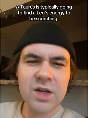 A close-up shot of a man wearing a black beanie, looking directly at the camera while speaking. Text overlay at the top reads: 'A Taurus is typically going to find a Leo's energy to be scorching.' The background is blurred, suggesting an indoor setting.