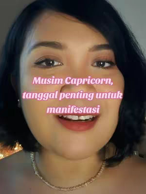 A close-up shot features a woman with dark hair smiling, framed from the chest up. The text overlayed reads 'Musim Capricorn, tanggal penting untuk manifestasi' in a pink font. She wears a necklace, and the background is out of focus.