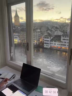 A window with a view of a cityscape. A laptop and a timer are on the windowsill.