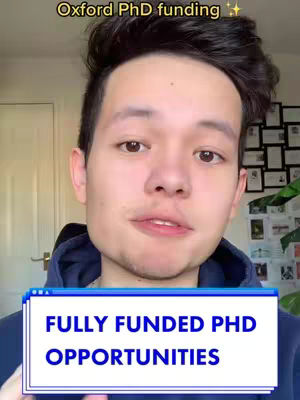 A young man is featured in a close-up, centered in the frame, with a blurred background of a room. He has dark hair and is wearing a navy blue hoodie. Overlaid on the image is a text box with the words 'FULLY FUNDED PHD OPPORTUNITIES' in white text against a blue and white background. Above the man's head, in a curve, the text 'Oxford PhD funding' is visible.