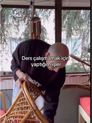 A bald man is seen leaning over, appearing to be cleaning a chair on a balcony. The balcony has a view through a window. Text overlayed on the image indicates the video is about 'the things I do to avoid studying'.