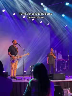 A live stage performance with a band. A man with a guitar is center, with a singer to his side. Stage lights create a dramatic atmosphere.