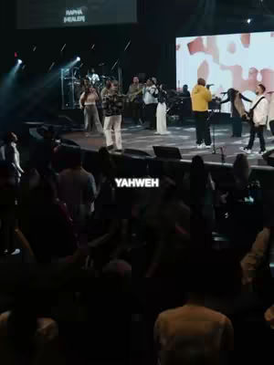 A live music performance on a stage. A group of people is singing and playing instruments on a stage with bright lights. Text overlay reads 'YAHWEH' at the bottom in bold white font.