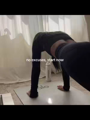 The image shows a person, likely a woman, bent over in a yoga pose on a mat. The person is wearing black workout clothes. The background features a white curtain and a water bottle. Text overlayed states: 'no excuses, start now'.