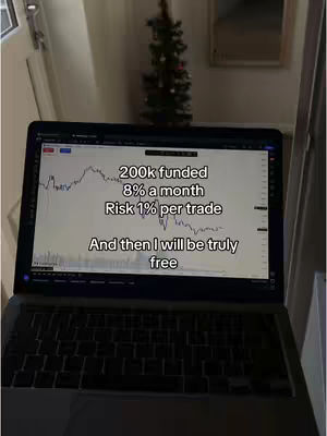 Laptop screen showing a trading chart with text overlay. The background includes a room and a small Christmas tree.