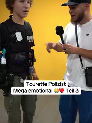 Two men are standing in front of a yellow background. One, on the left, is wearing a vest, the other is holding a microphone. Text overlays the image.