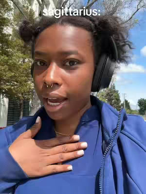 A selfie-style video shows a Black woman with her hair styled up, wearing headphones, and a blue jacket. She is outdoors on a sunny day with trees in the background. The text overlay says "sagittarius:" in a white font.