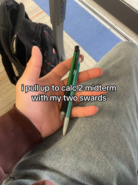 The cover image shows a person's hand holding two pens, possibly mechanical pencils, against a backdrop of crossed legs in denim jeans. Text overlayed on the image reads, 'i pull up to calc 2 midterm with my two swsards'. The image has a casual, real-life feel, with a focus on the pens and the legs. The hand holding the pens takes center stage, while the denim jeans provide a neutral background.