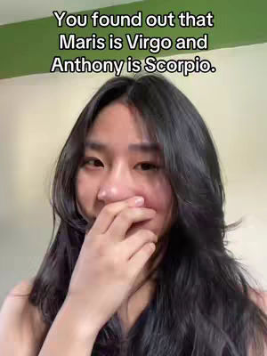 A woman with long, dark hair is shown from the chest up, covering her mouth with her right hand. The background appears to be an indoor setting with a green wall and a lighter wall. The text overlay reads, “You found out that Maris is Virgo and Anthony is Scorpio.”