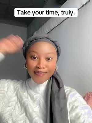 A smiling young woman with a grey headscarf and a white sweater is featured. The background is a light-grey wall with textured detail. The text overlay says 'Take your time, truly.'