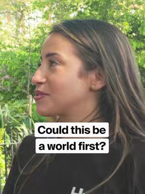 A woman in profile is seen in a medium shot, set against a blurred green background likely outdoors. She has light skin, medium-length brown hair with lighter highlights, and is wearing a black top. Overlayed on the image are two white rectangles with the text: "Could this be a world first?" in a dark, sans-serif font.