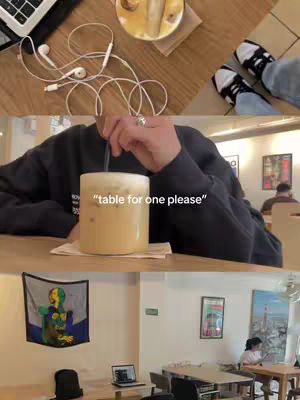 The cover image is a split view. The top half shows a wooden table setting with a laptop, eyeglasses, earbuds, and shoes. The bottom half shows a person holding a straw in a large yellow drink with the text overlay "table for one please" in the middle.