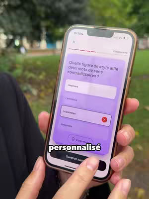 A hand holding a smartphone displaying a quiz question on a purple background with options to answer. The phone has a gold frame and is in front of a blurry outdoor setting.