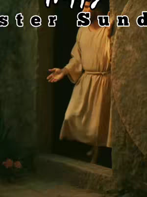 The image shows Jesus emerging from a tomb. He is wearing a tan robe and has his arm outstretched as if gesturing. The tomb is open, with stone walls and a stone floor. Soft, warm light is illuminating everything.