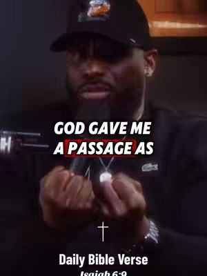 The image is a medium shot of a Black man wearing a black cap and a black outfit, centered in the frame. Text overlays are placed on the image, including "GOD GAVE ME A PASSAGE AS" with a red box around the word PASSAGE, and a section at the bottom that reads "Daily Bible Verse Isaiah 6:9" set against a dark background. A silver cross is also present.