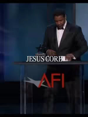 The image shows a man in a suit and bow tie speaking at a podium. The background is a teal color. Overlayed on the image is the text JESUS CORE in white font.