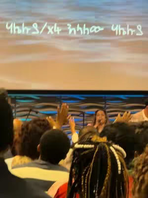 The cover image shows a stage with a choir singing. In the foreground, the backs of audience members are visible, raising their hands. A singer stands at a microphone, and text is overlaid at the top.