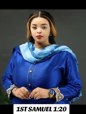The image features a woman in a royal blue outfit, possibly a dress or top and pants set. She has on a blue scarf and is adorned with jewelry, including a watch. The background is a muted gray.