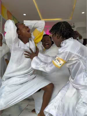A group of people are huddled in what appears to be a church setting. Most are wearing white robes. The subjects are reacting to something, showing expressive faces; some are shielding each other.
