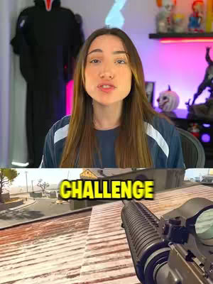 A selfie video showing a woman in a blue shirt looking at the camera and a game in the background.