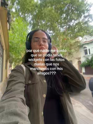 A selfie-style video cover image featuring a young woman wearing glasses and headphones, set against a blurred outdoor background of greenery. The woman is centered in the frame, with her head and shoulders visible. The background suggests a residential or urban environment. Text overlayed on the image is in Spanish.