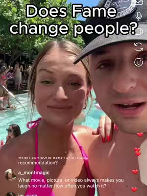 A selfie-style shot featuring a woman and a man, both smiling while posed in front of a blurred background with a pool and greenery, suggesting an outdoor setting. The woman wears a pink top, and the man has a black cap. Text overlaid at the top asks a question.
