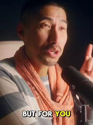 A man is speaking into a microphone. He is wearing a gray shirt under a striped sweater and an orange scarf. The words "BUT FOR YOU" are shown as text overlaid on the image with a yellow highlight.