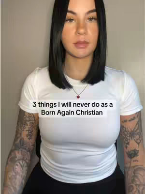 A woman with dark hair and tattoos on her arms is centered in the frame. She is wearing a white t-shirt and a small heart pendant necklace. Text overlayed on the image reads '3 things I will never do as a Born Again Christian'.