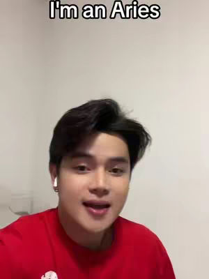 A young man with dark hair and a red shirt is centered in the frame, speaking towards the camera. Above him, the text overlay "I'm an Aries" is displayed in a bold, white font. The background is a plain white wall.