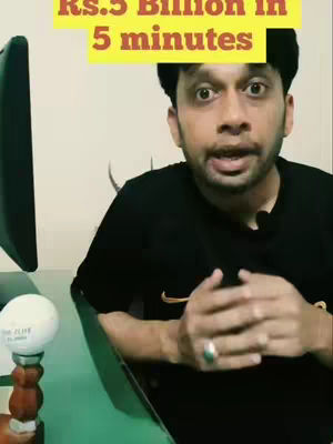 A man with short, dark hair and brown eyes is speaking into a microphone. He's wearing a black shirt and has a ring on his finger. In the upper center of the image, a yellow rectangle contains white text. Behind him is a computer monitor, and a portion of a green table is visible.
